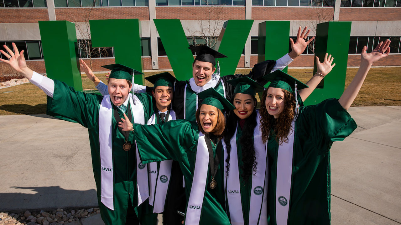 A group of UVU graduates standing in front of a UVU sign